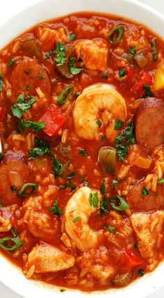 a white bowl filled with shrimp, sausage and tomato soup on top of a table