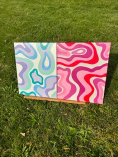 two colorful paintings sitting on top of a lush green field