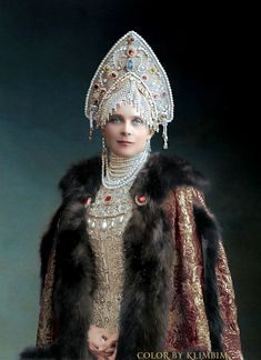 a woman dressed in an elaborate costume with fur and jewels on her head, standing against a dark background