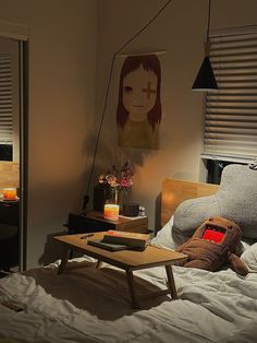 a teddy bear sitting on top of a bed next to a wooden table with candles