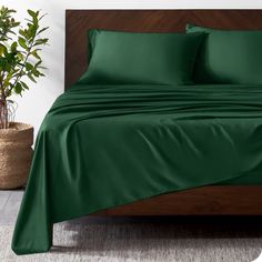 a bed with green sheets and pillows in a room next to a potted plant