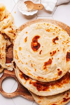 three tortillas on a wooden cutting board next to a knife and some other food