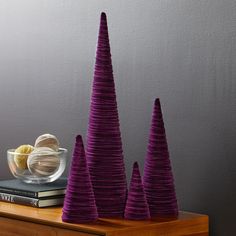 three purple cones sitting on top of a wooden table next to a bowl of fruit