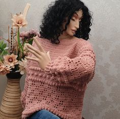 a mannequin sitting next to a vase with flowers in it and wearing a pink sweater