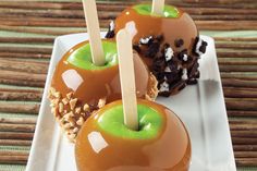 two caramel apples with chocolate and sprinkles on a square white plate