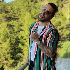 a man in striped shirt and sunglasses standing on top of a wooden platform with trees behind him