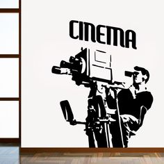 a black and white photo of a man holding a camera in front of a wall with the word cinema on it