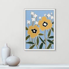 a white vase sitting on top of a table next to a framed art print with yellow and black flowers