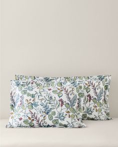 two pillows sitting on top of a bed with white sheets and green plants in them