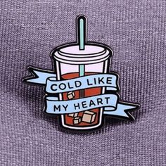 a pin with the words cold like my heart on it and a drink in front