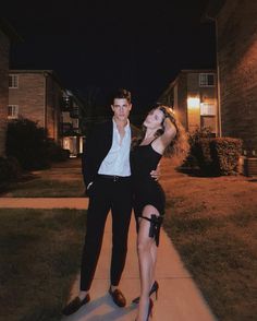 a man and woman posing for a photo in front of a house at night with their arms around each other