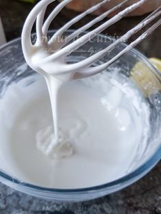 the whisk is being poured into the bowl with white liquid and lemon wedges