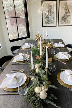 a dining room table set for christmas with gold and white plates, silverware, greenery and candlesticks