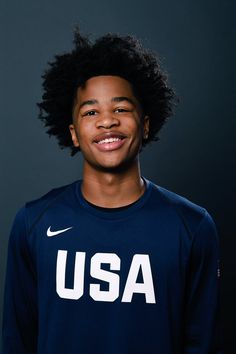 a young man wearing a usa shirt and smiling for the camera in front of a dark background