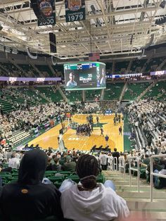 people sitting in the bleachers watching a basketball game on an indoor court with lots of green seats