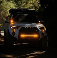 the front end of a white suv driving down a forest road at night with its lights on