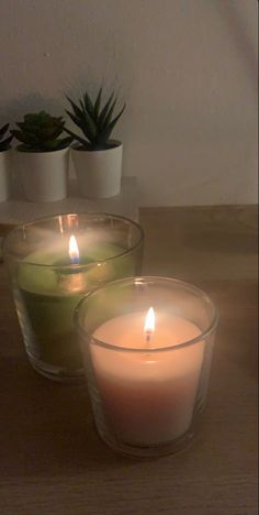 three lit candles sitting on top of a wooden table next to succulents