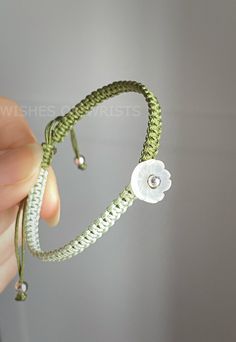 a hand holding a green string bracelet with a white flower on the end and a bead in the middle