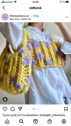 a knitted yellow purse with purple flowers on the front and bottom, attached to a white shirt