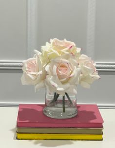 a glass vase filled with pink and white flowers on top of a stack of books