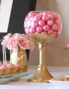 there is a vase with pink balls in it and some cupcakes on the table