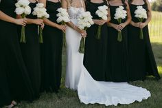 a group of women standing next to each other in black dresses and holding bouquets