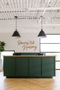 the reception desk is green and has black lamps hanging from it's ceiling above