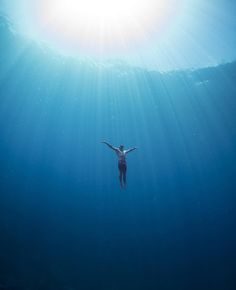 a person swimming in the ocean with their arms spread out and sun shining over them