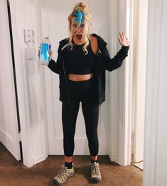 a woman in black top and leggings standing next to door with water bottle