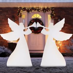 two lighted angel figurines in front of a house with christmas wreath on the door