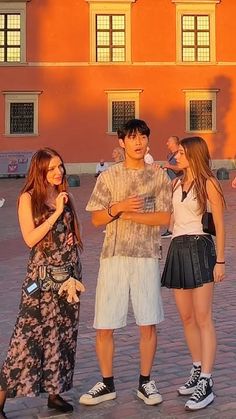 three young people are standing in front of an orange building and talking to each other