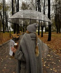 a woman is walking in the rain with an umbrella over her head and holding a book