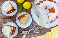 three plates with slices of cake on them next to lemons and a cutting board