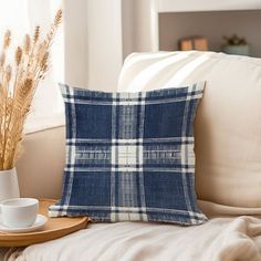 a blue and white plaid pillow sitting on top of a couch next to a cup