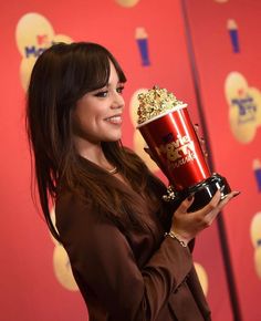 a woman holding a popcorn bucket and posing for the camera in front of a red wall