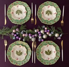 the table is set for christmas dinner with silverware and green plates, holly decorations