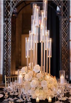 a tall centerpiece with candles and flowers on a black table cloth in front of a chandelier