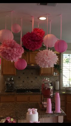 pink and red paper flowers hanging from the ceiling above a kitchen counter with cakes on it