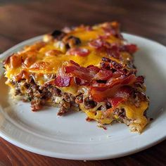 a slice of breakfast casserole on a white plate with bacon, cheese and other toppings