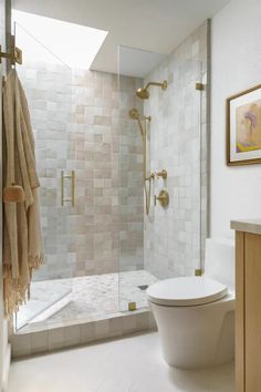 a white toilet sitting next to a shower in a bathroom under a window with gold fixtures