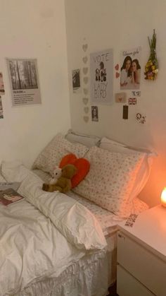 a bed with white sheets, pillows and a teddy bear on it next to a night stand