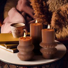 three candles sitting on top of a table next to books and a cup of coffee