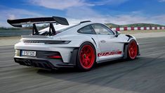 a white sports car driving on a race track with red rims and wing extensions