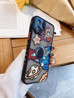 a person holding up a phone case with cartoon characters on it, and an open book in the background