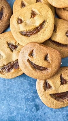 a pile of cookies with faces drawn on them sitting on a blue table top next to each other