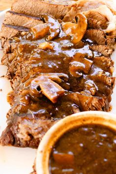 a white plate topped with meat and gravy next to a cup of sauce