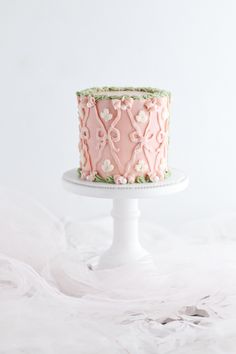 a pink and green cake sitting on top of a white cake platter with flowers