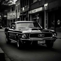 a black and white photo of an old mustang on the street in front of a building