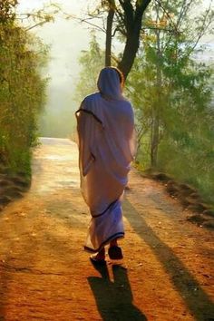 a person walking down a dirt road with a white robe over their head and hood on