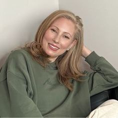 a woman sitting in a chair with her hand on her head and smiling at the camera